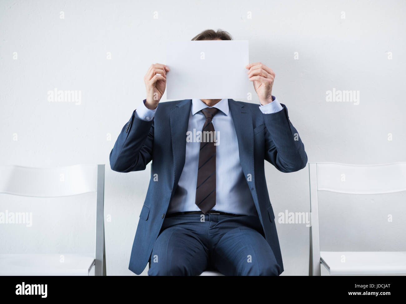 Imprenditore che ricopre la faccia con la carta mentre è seduto su una sedia Foto Stock