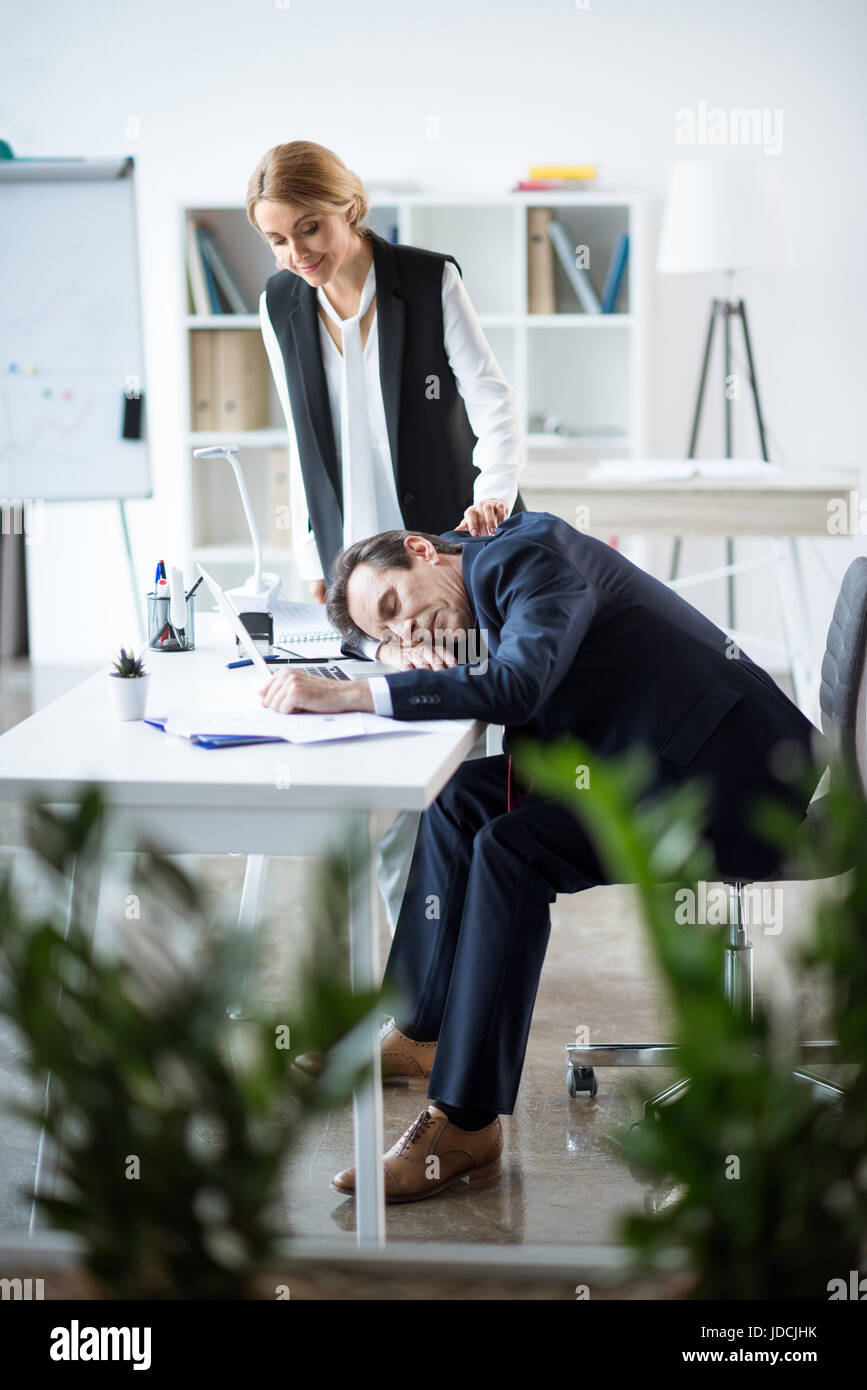 Sorridente imprenditrice guardando imprenditore a dormire sul posto di lavoro Foto Stock