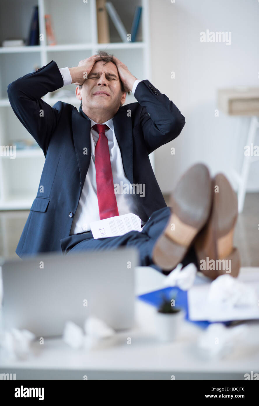 Sottolineato imprenditore maturo seduta a tavola con laptop e gesti Foto Stock