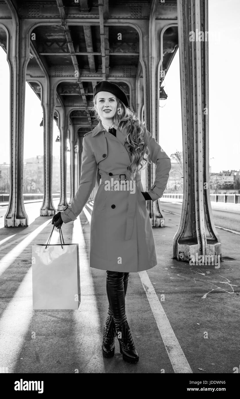 Luminose a Parigi. A piena lunghezza Ritratto di giovane viaggiatore woman in red trench coat sul Pont de Bir-Hakeim bridge in Paris holding shopping bag Foto Stock