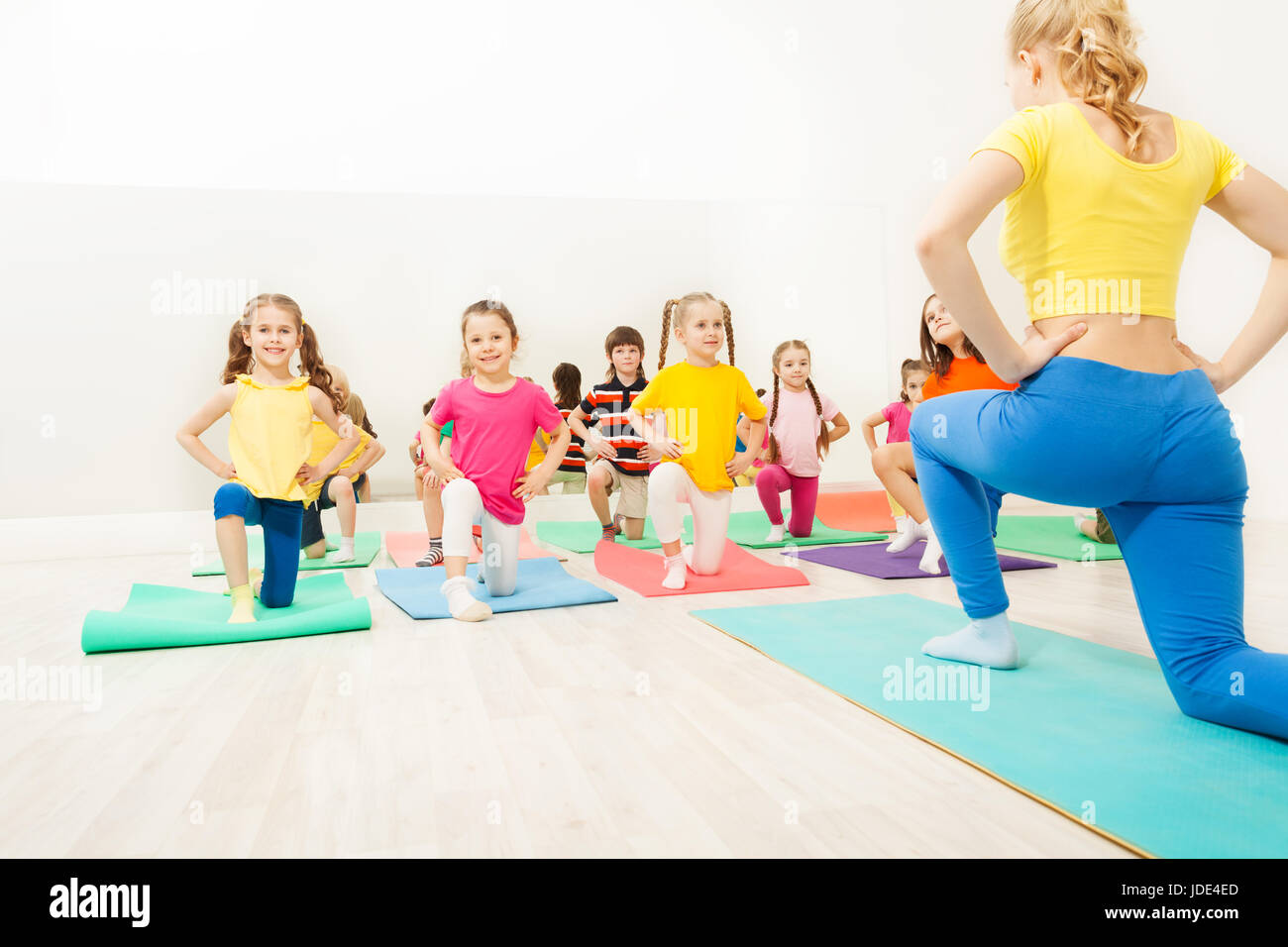 Gruppo di contenti i bambini a fare gli esercizi in palestra con la ginnastica femminile coach Foto Stock