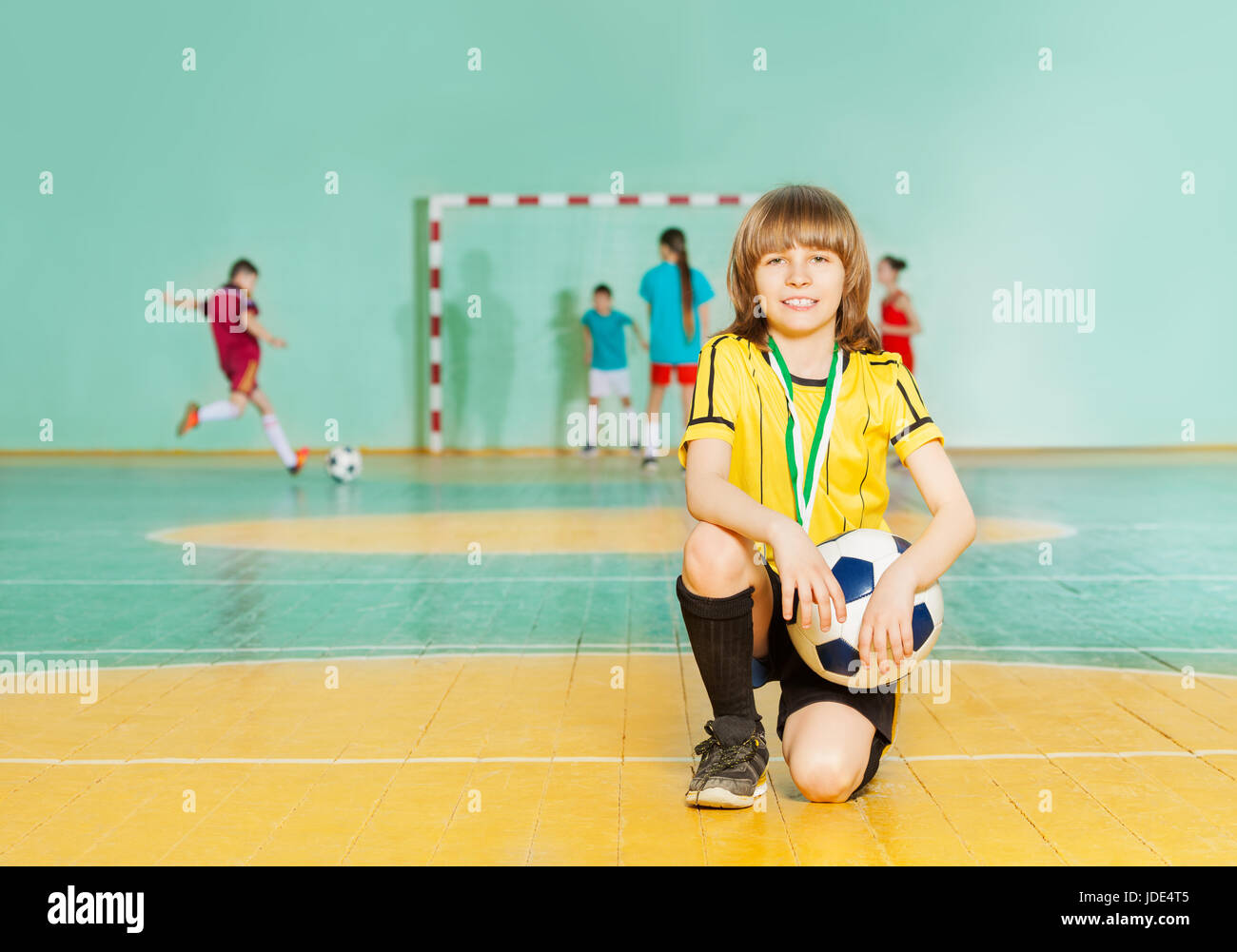 Ritratto di sorridere preteen boy, soccer team capitano, in piedi sul ginocchio di futsal con sfera Foto Stock