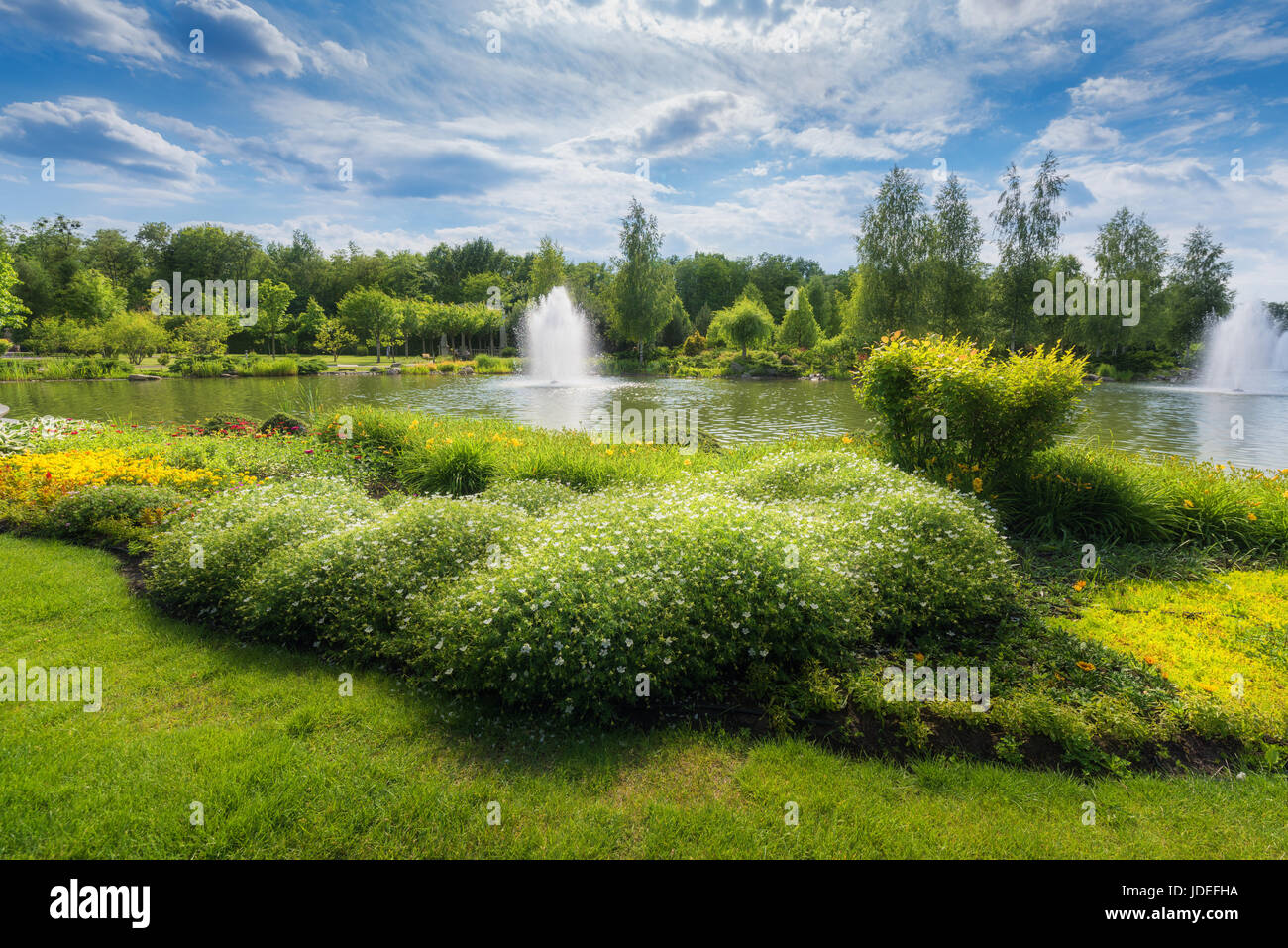 Bellissima vista del Parco in estate in Mezhyhirya, Ucraina. Paesaggio colorato con erba verde, fiori, alberi, fontana, stagno e cielo blu con clo Foto Stock