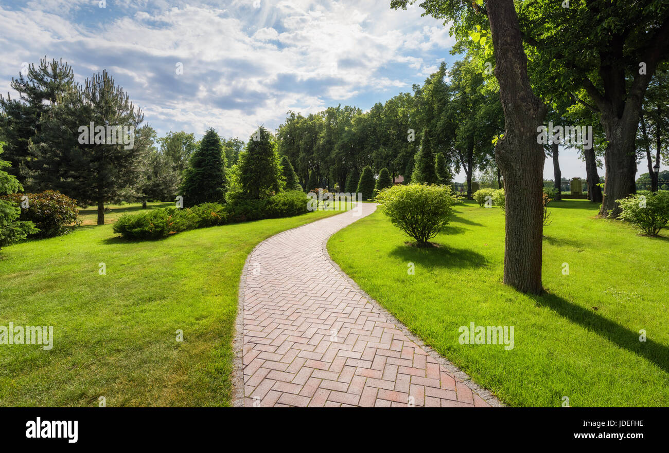 Bellissima vista del fantastico parco in estate in Mezhyhirya, Ucraina. Paesaggio colorato con erba verde, il percorso, piante, alberi e cielo blu con nuvole Foto Stock