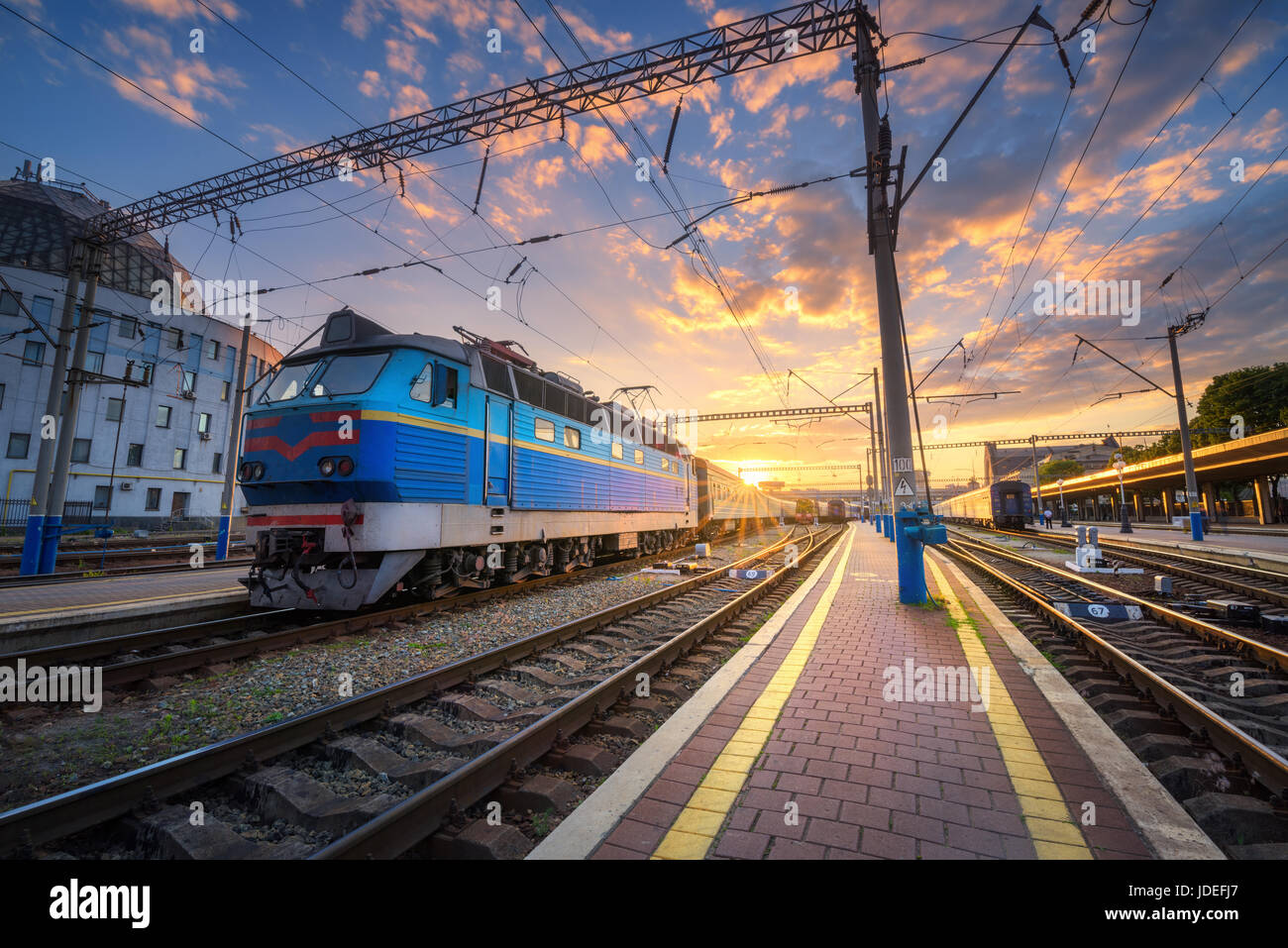 Treno Blu presso la stazione ferroviaria al tramonto. Incredibile paesaggio industriale con la vecchia locomotiva, edifici, rotaie e colorato tramonto Cielo con nuvole. T Foto Stock