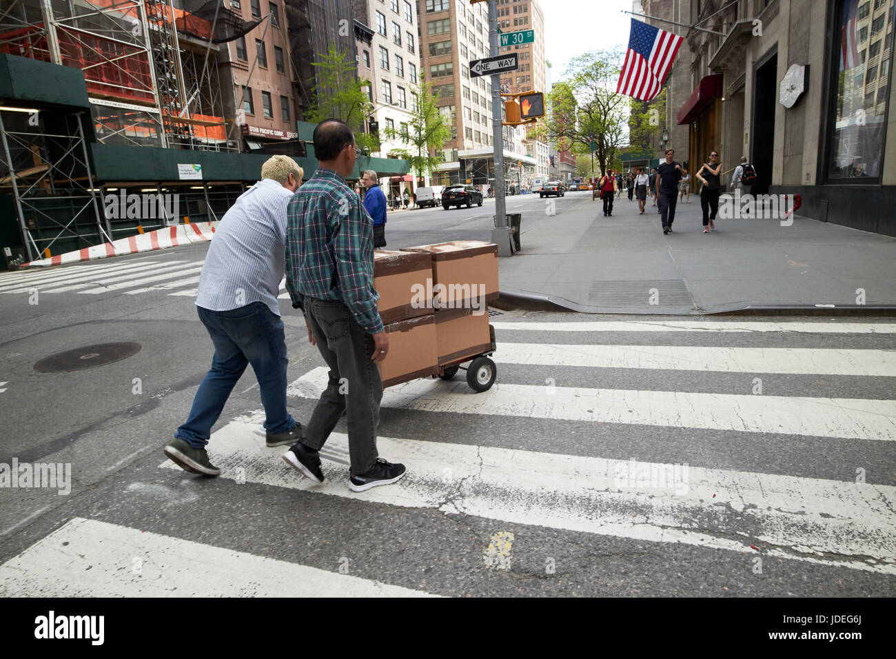 Gli uomini spingendo il carrello consegna attraverso crosswalk nel centro di Midtown New York City USA Foto Stock