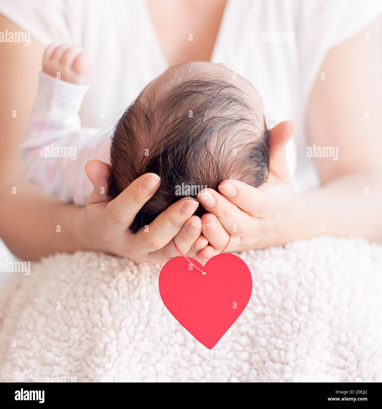 Madre tenendo la testa del suo neonato in mani. Happy family concept. Amore Materno e amore parentale. Cuore rosso appesi ai bracci. Foto Stock
