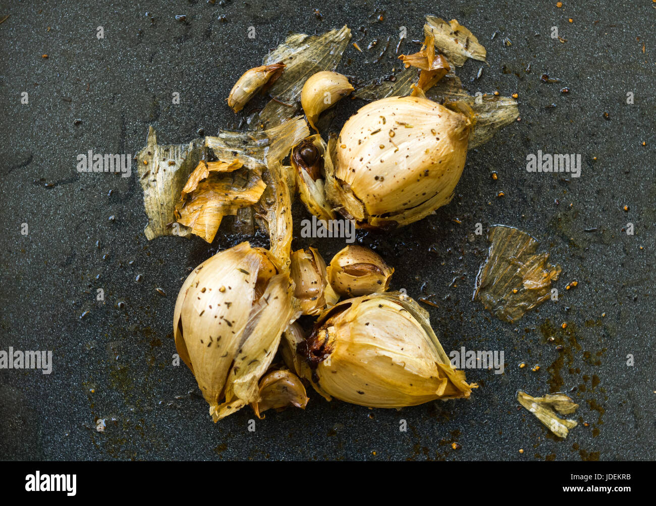 Caramellizzato tostato aglio fresco di forno su un colore blu acciaio vassoio cosparso di rosmarino essiccato e timo Foto Stock