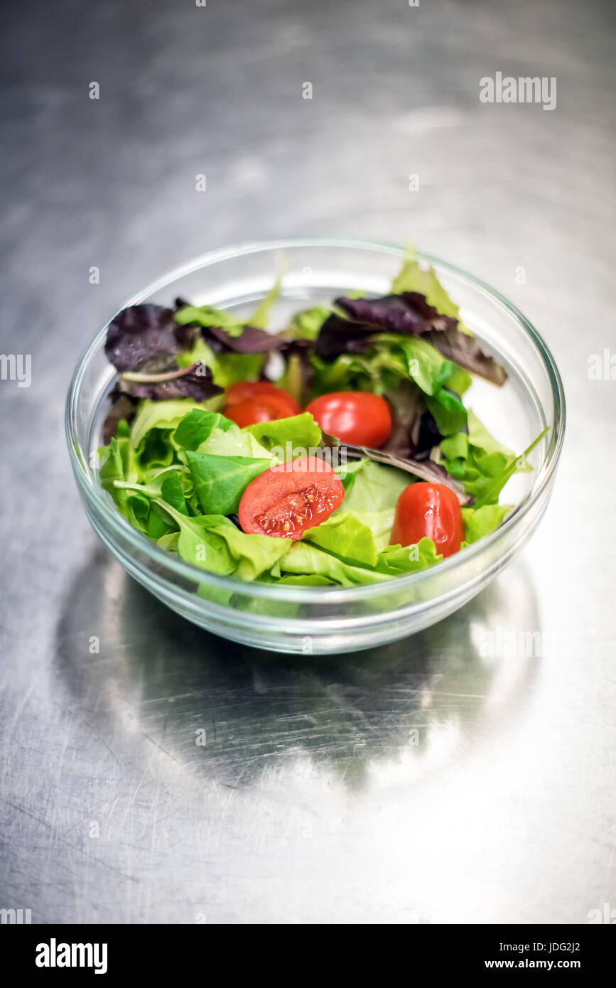 Pronto misti foglia verde con insalata di pomodori tagliati a cubetti in una ciotola di vetro pronti per essere serviti come accompagnamento o contorno per un pasto Foto Stock