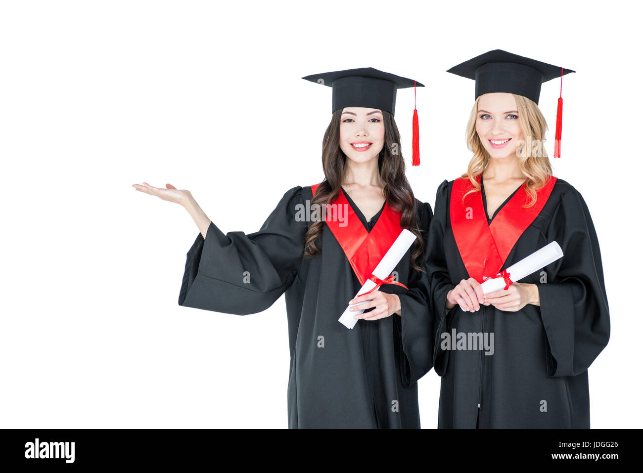 Due belle giovani studenti di cappucci accademico tenendo diplomi e sorridente in telecamera Foto Stock