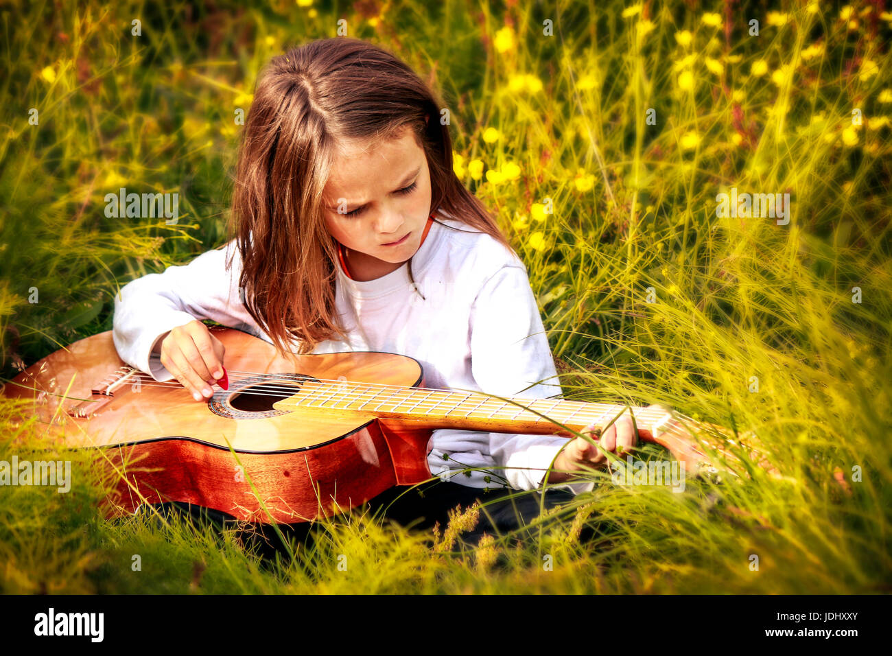 Bambino seduto nell'erba alta a suonare la chitarra Foto Stock