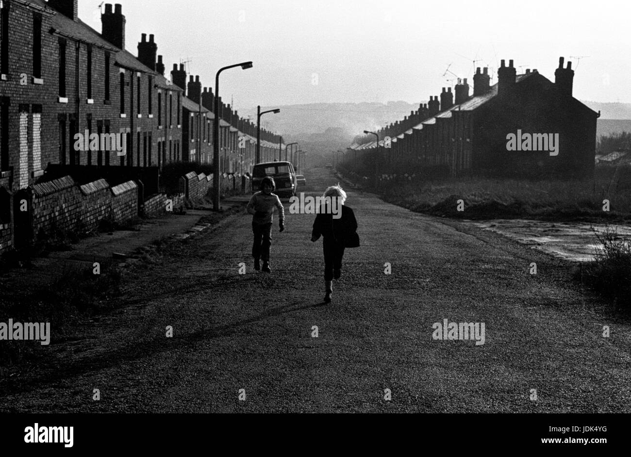 Immagine in bianco e nero di due bambini che camminano lungo una strada a schiera vuota in una città post-industriale del Regno Unito, catturando la vita urbana e la storia della classe operaia Foto Stock