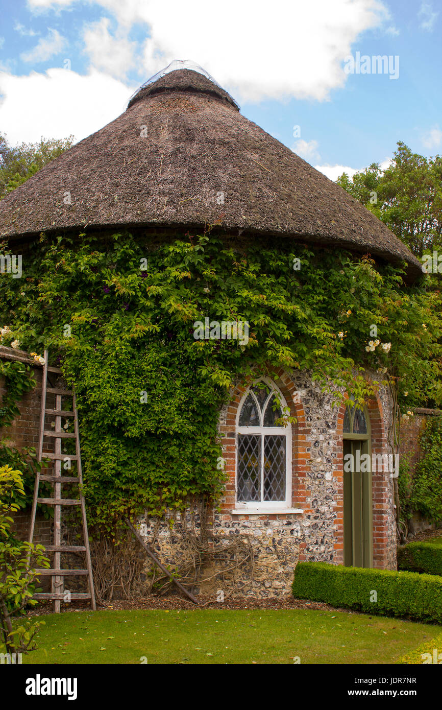 Il XIX secolo con tetto di paglia di casa rotonda circondata da bellissime aiuole e sentieri di ghiaia in il giardino murato a West Dean Gardens nel West Sussex, E Foto Stock