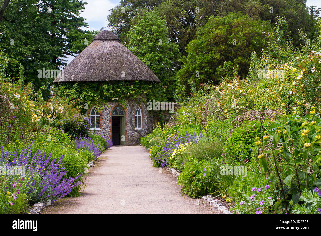 Il XIX secolo con tetto di paglia di casa rotonda circondata da bellissime aiuole e sentieri di ghiaia in il giardino murato a West Dean Gardens nel West Sussex, E Foto Stock