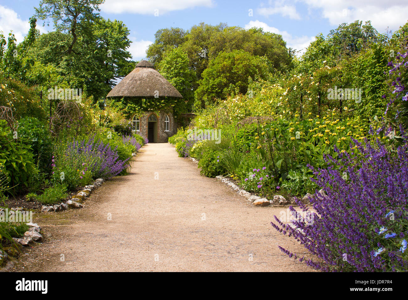 Il XIX secolo con tetto di paglia di casa rotonda circondata da bellissime aiuole e sentieri di ghiaia in il giardino murato a West Dean Gardens in West Sussex Foto Stock