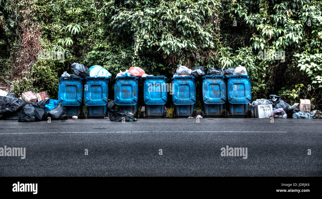 Una fila di bidoni della spazzatura rivestita traboccante a lato della strada Foto Stock