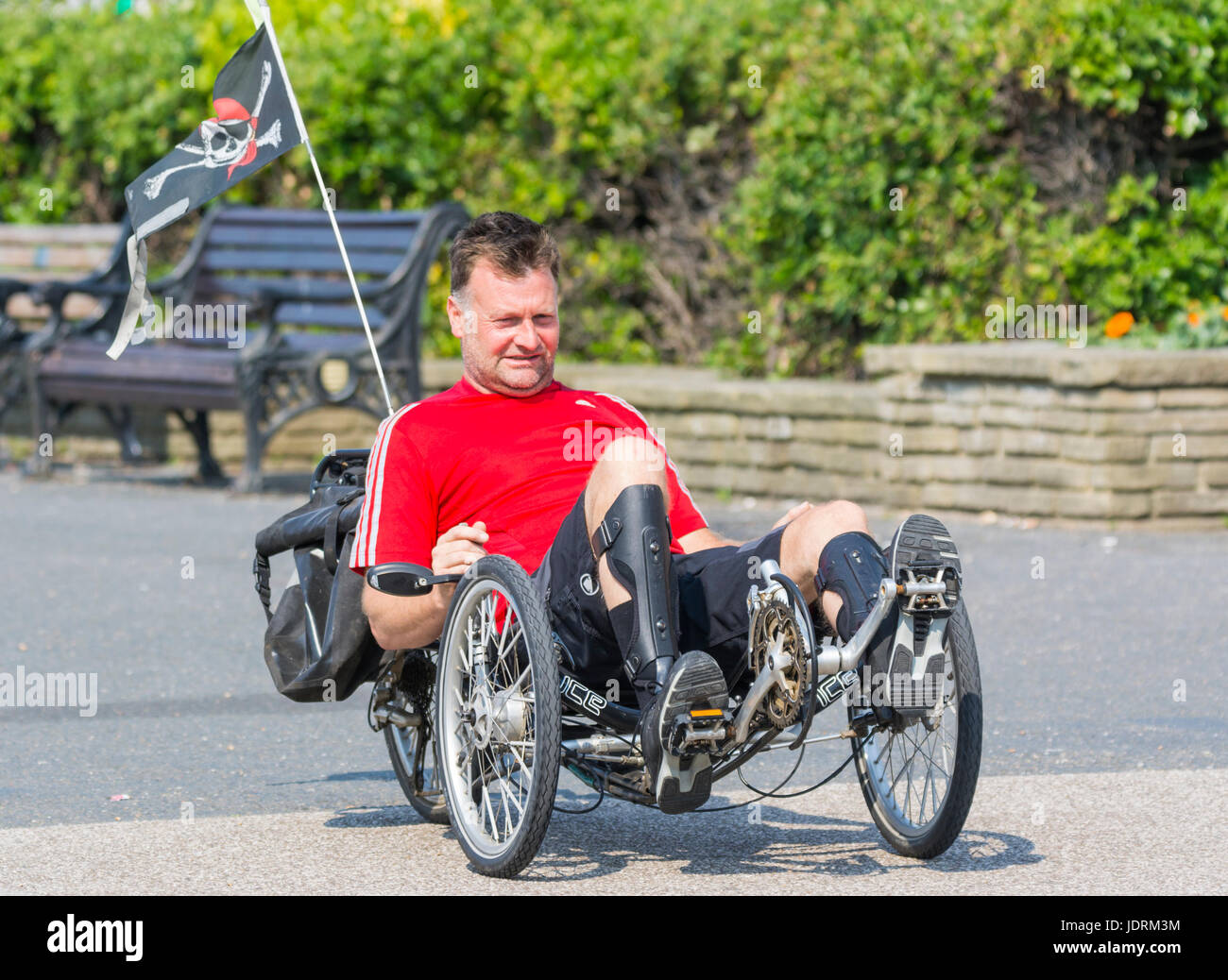 Uomo a cavallo di un ergometro orizzontale lungo una passeggiata sul lungomare in una giornata calda. Foto Stock Uomo a cavallo di un ergometro orizzontale lungo una passeggiata sul lungomare in una giornata calda. Foto Stock