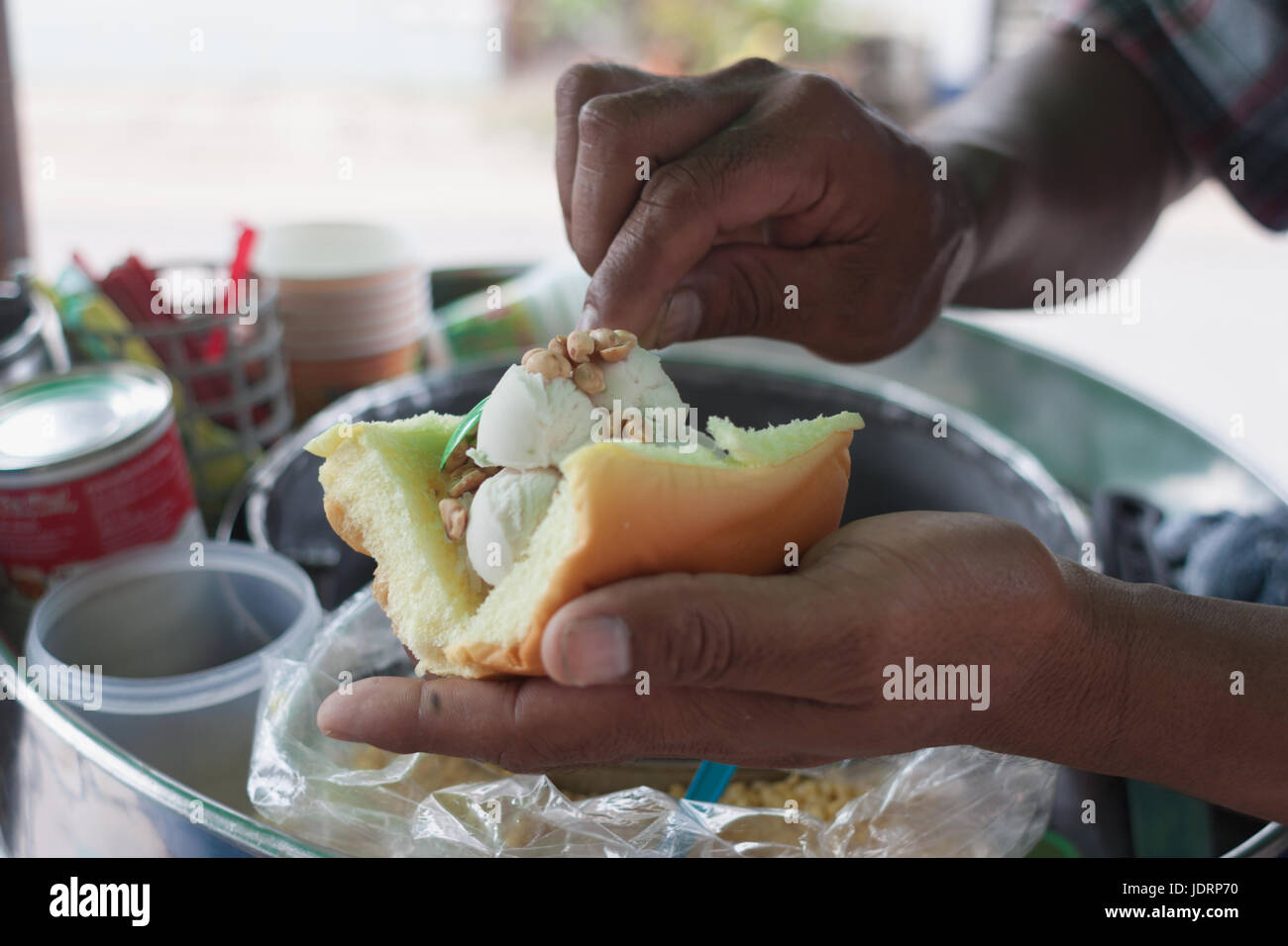 Saler scooping gelato al cocco e rabboccato con arachidi e latte medicazione sul pane.tradizionale gelato al cocco in Thailandia Foto Stock