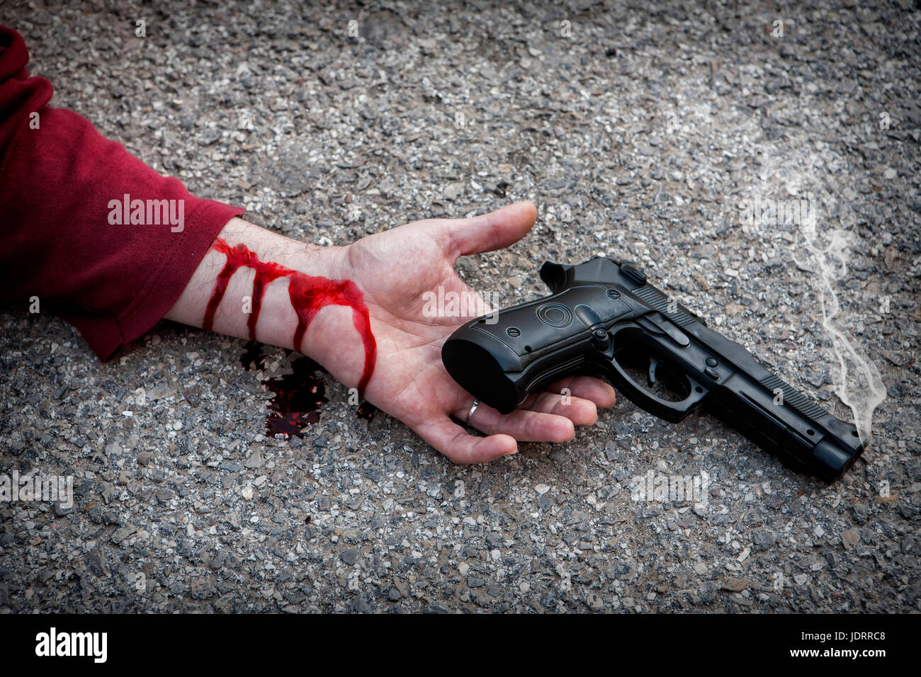 L'uomo con la pistola in mano insanguinata giace morto nell'asfalto vittima di omicidio Foto Stock