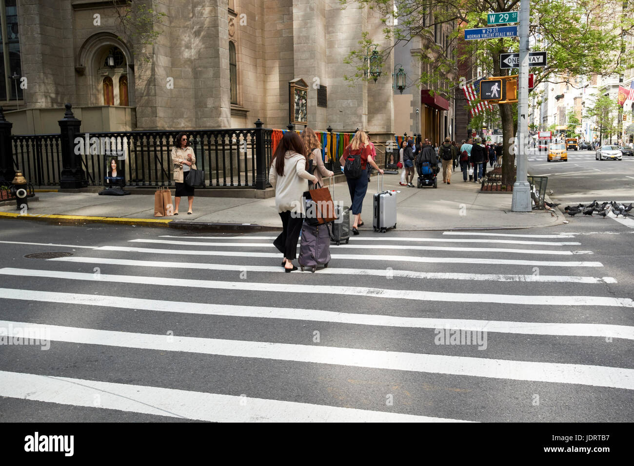 Tre donne con Borsoni con ruote attraversando crosswalk sulla Fifth Avenue di New York City STATI UNITI D'AMERICA Foto Stock