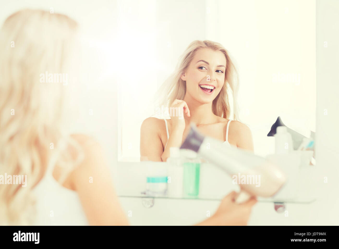 Felice giovane donna con ventola di asciugatura capelli in bagno Foto stock  - Alamy