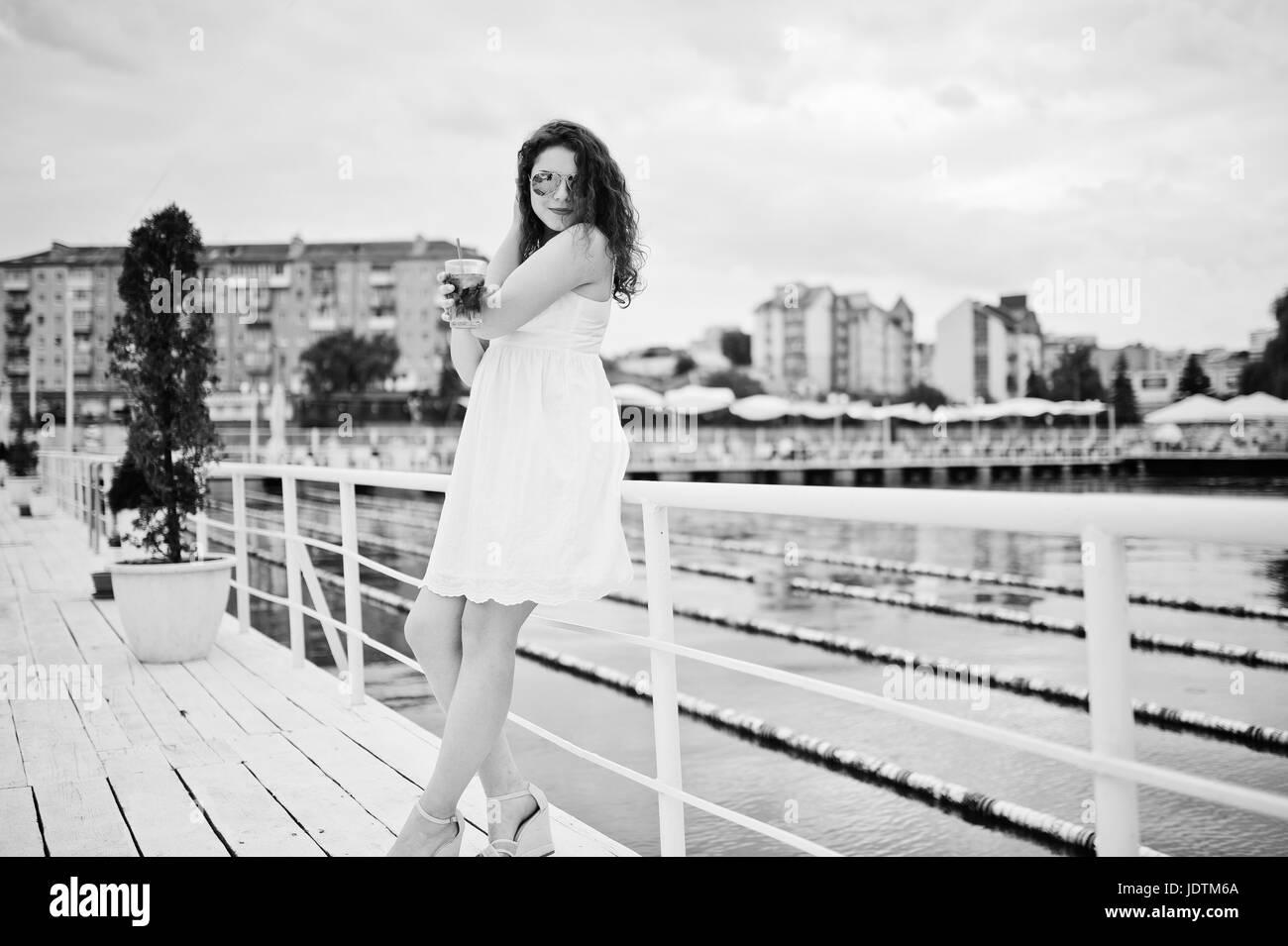 Ritratto di un attraente giovane donna in posa con il suo cocktail su un lago indossando occhiali da sole. Foto in bianco e nero. Foto Stock