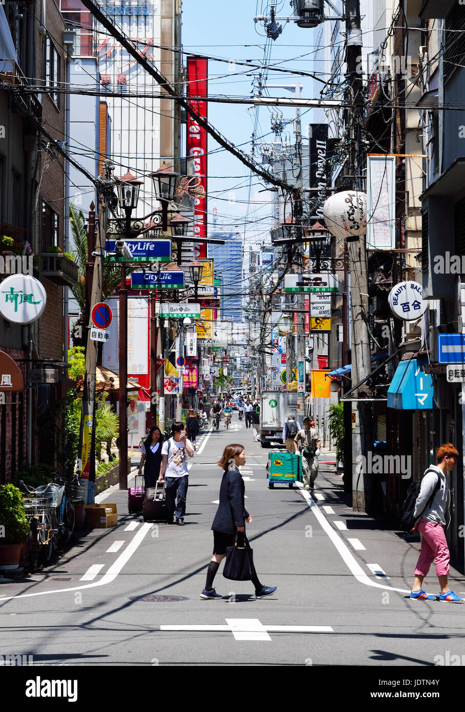 Un ufficio giapponese donna attraversa la strada di fronte a un vicolo stretto nel quartiere Namba di Osaka, Giappone Foto Stock