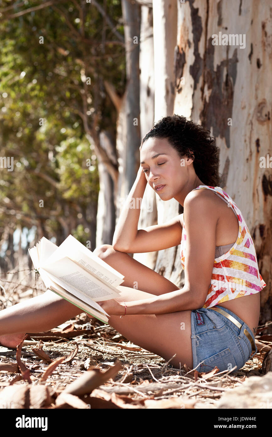 Giovane donna seduta al piede della struttura ad albero del libro di lettura Foto Stock