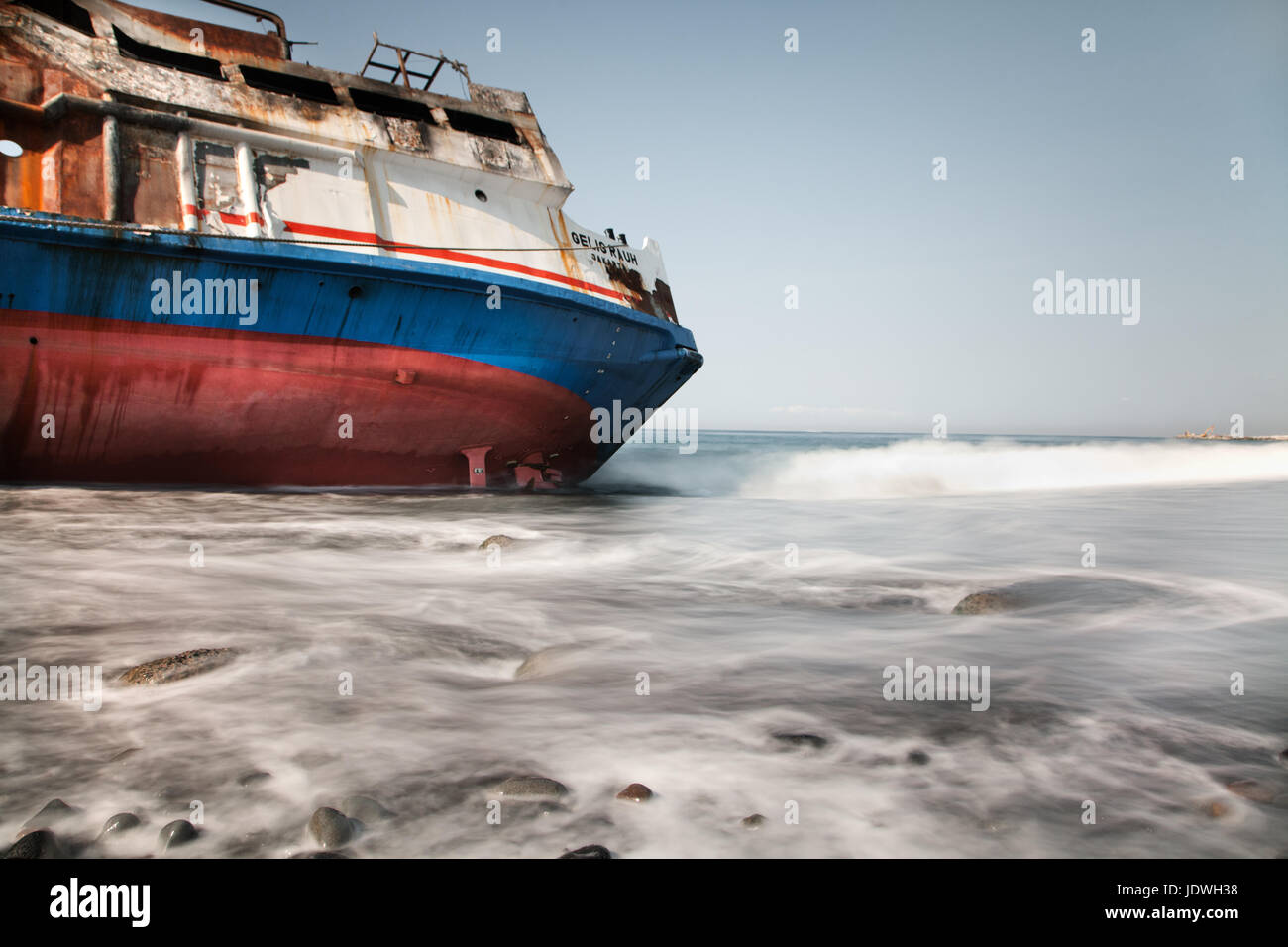 Naufragio barca in riva al mare sulla isola di Bali prese con esposizione a lungo per creare un bellissimo effetto con la marea che accarezzano la barca Foto Stock