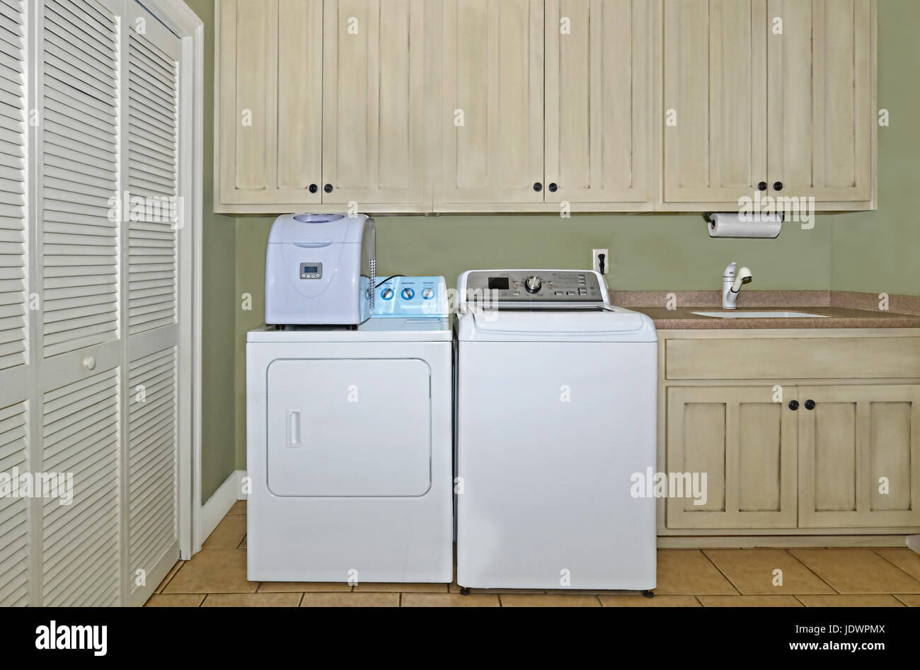 Una sala lavanderia con lavatrice, asciugatrice,fabbricatore di ghiaccio,lavabo,armadi,e un area dispensa. Gli armadietti hanno una leggera finitura anticato su di essi. Foto Stock