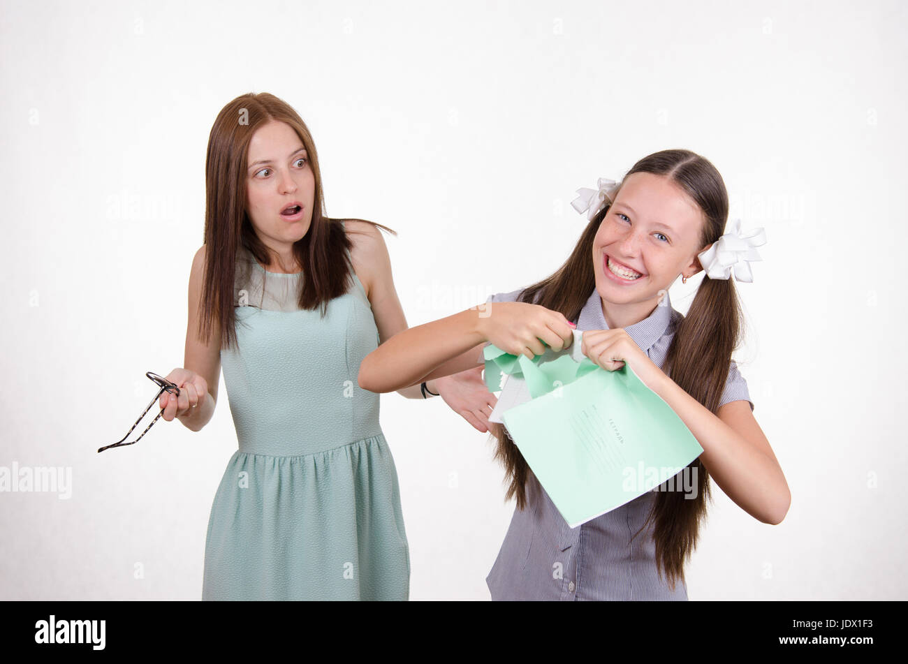 Schoolgirl divertendosi di strappare il notebook nella parte anteriore di un insegnante arrabbiato Foto Stock