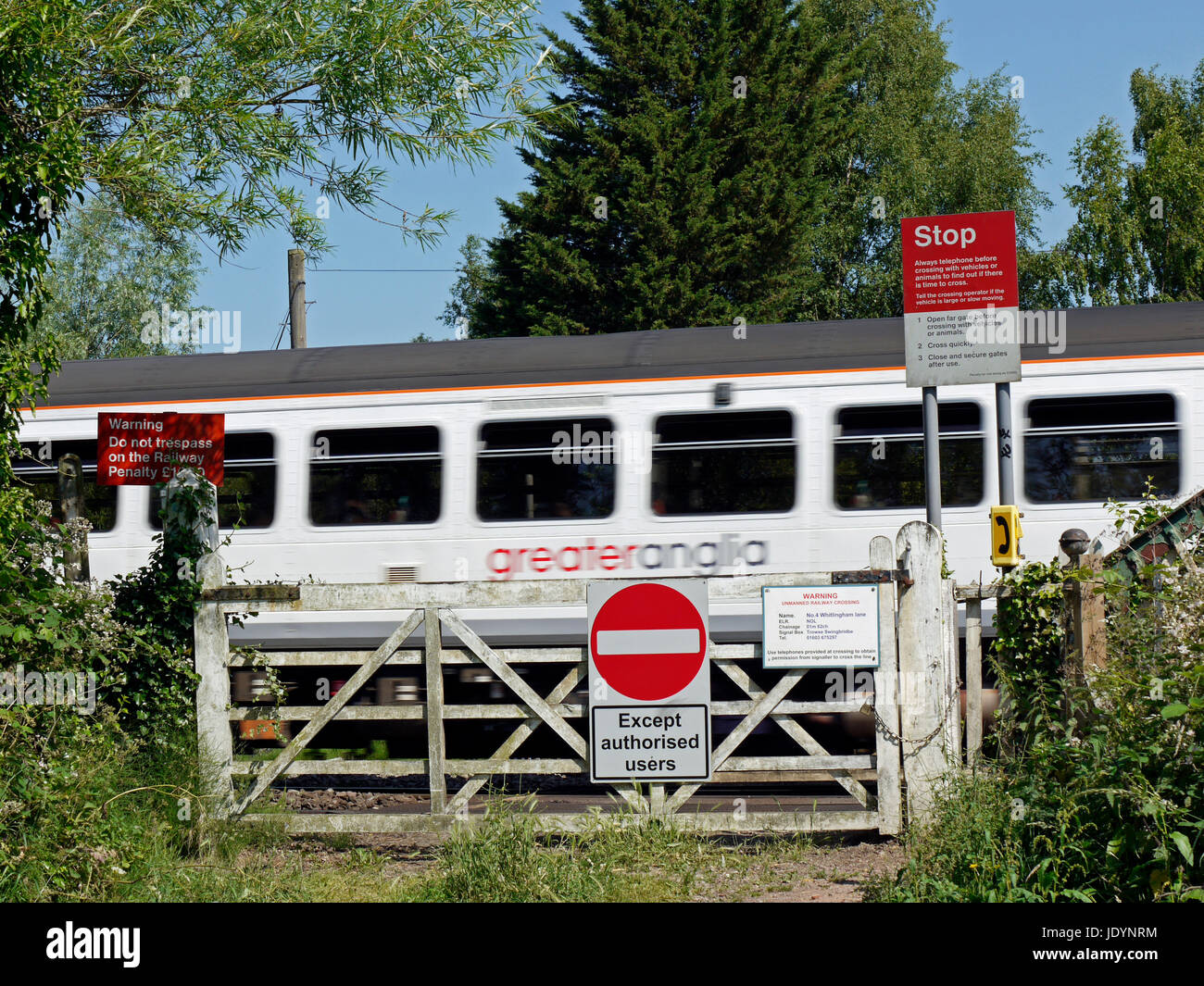 Una maggiore Anglia treno regionale con attraversamento di un vecchio passaggio a livello con cartelli di avvertimento ad est di Norwich, Norfolk, Inghilterra, Regno Unito Foto Stock
