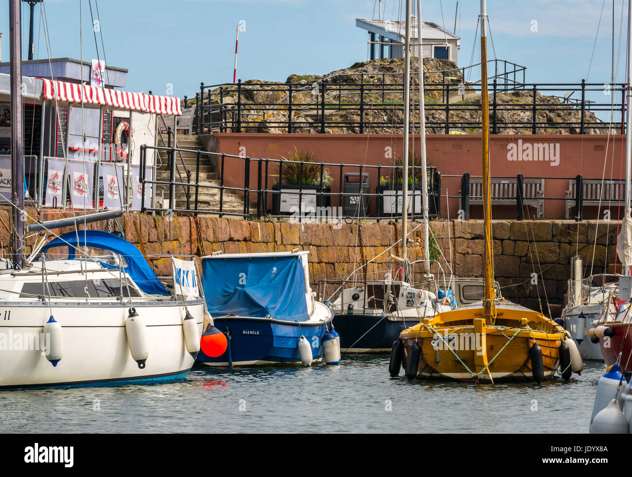 Barche a vela ormeggiata in North Berwick Harbour, East Lothian, Scozia, con la barca di legno e aragosta shack sul lato banchina con cielo blu Foto Stock
