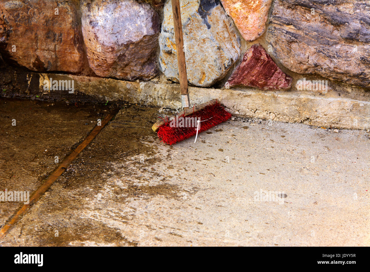 Un vecchio e sporco spazzola scopa sorge nei pressi del muro di pietra Foto Stock