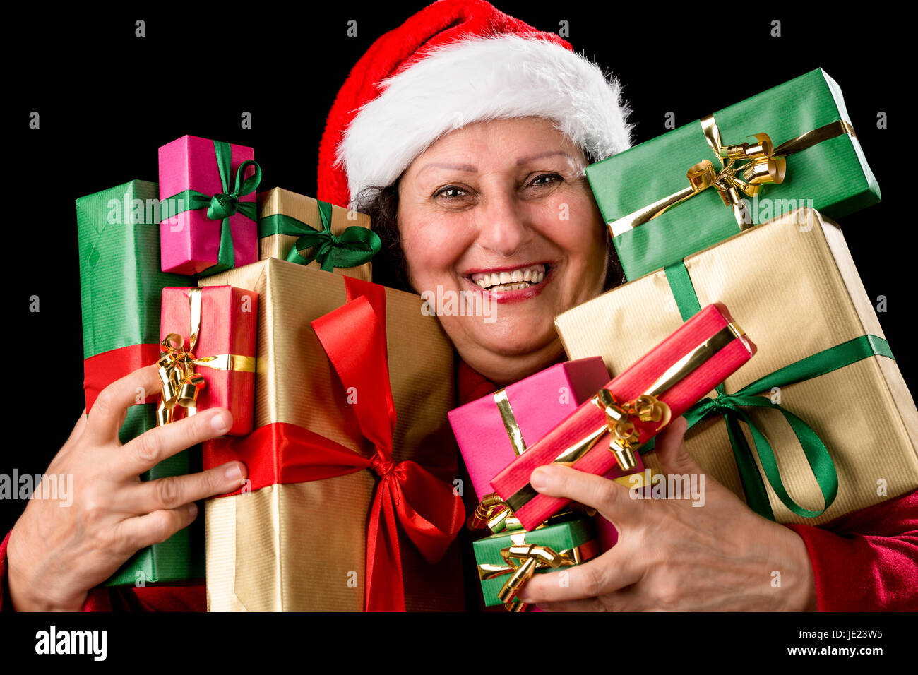 Onorevole deputata ricolma di gioia è la pressatura dieci avvolto regali di Natale al petto. Santa Claus hat e ricoprire i. Denti sorridente. Isolato su nero. Dicembre tema. Rosso, verde e golden doni. Foto Stock