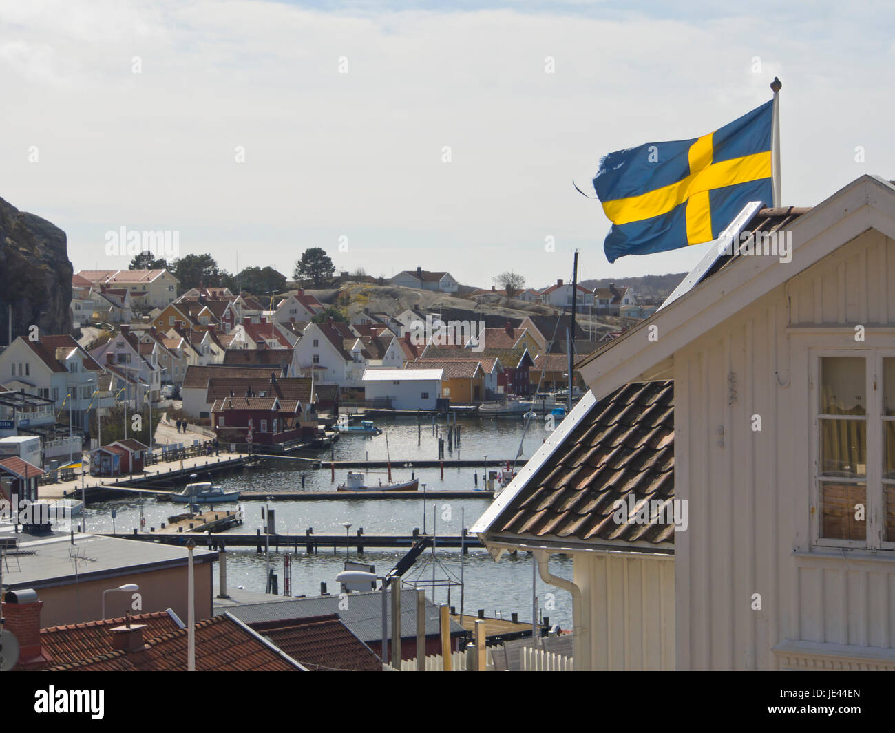 La piccola città di Fjallbacka sulla costa occidentale della Svezia, una destinazione di vacanza, vista del porto e marina, bandiera svedese sventola sui tetti Foto Stock