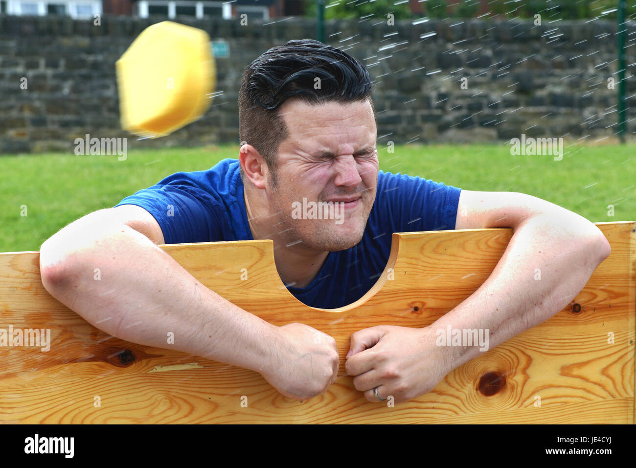 Un uomo in stock di legno ha una spugna bagnata gettato a lui in un tradizionale British Summer Fair. Foto Stock