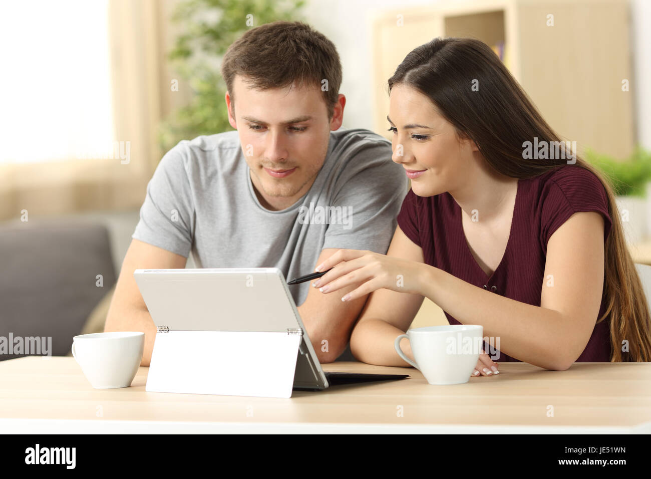 Matura la ricerca on line il contenuto con un tablet pc seduti a un tavolo nel soggiorno di casa con una finestra in background Foto Stock
