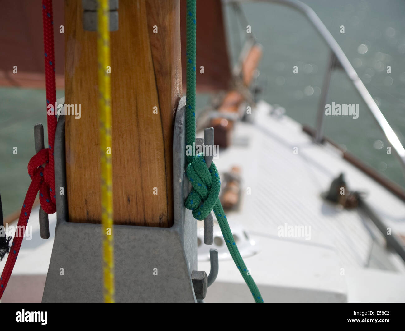 Close up di colore rosso e verde funi legate ordinatamente intorno bitte su un montante di yacht. Foto Stock