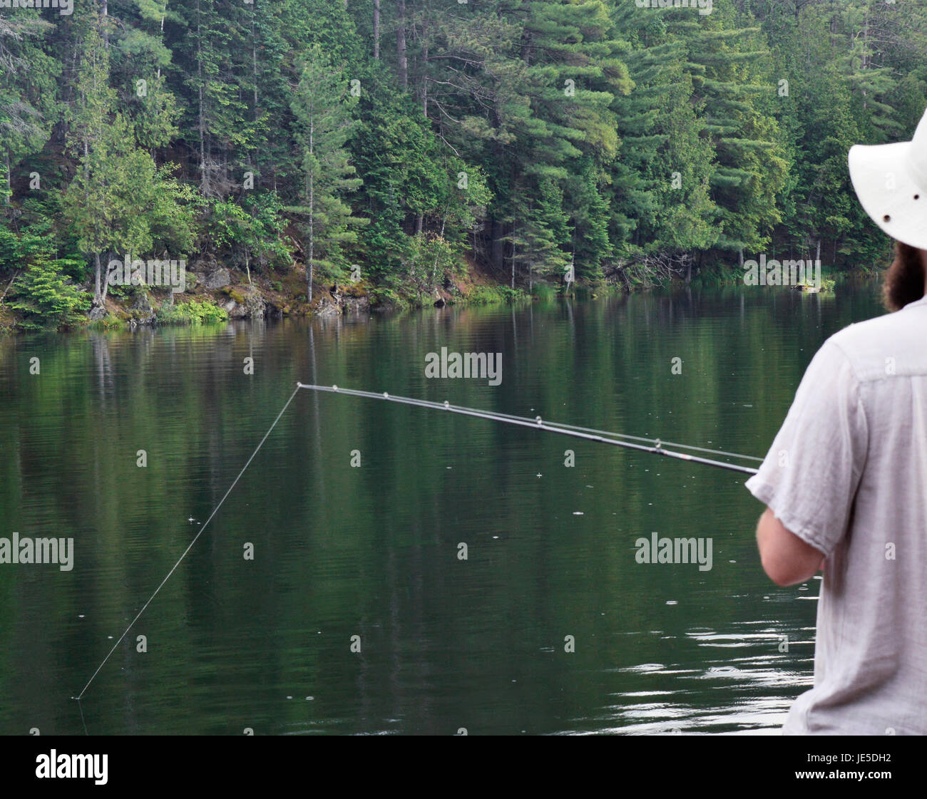 Casting chiamata! Un pescatore proietta una linea nelle calme acque del lago per la speranza di un morso o la cena. Foto Stock