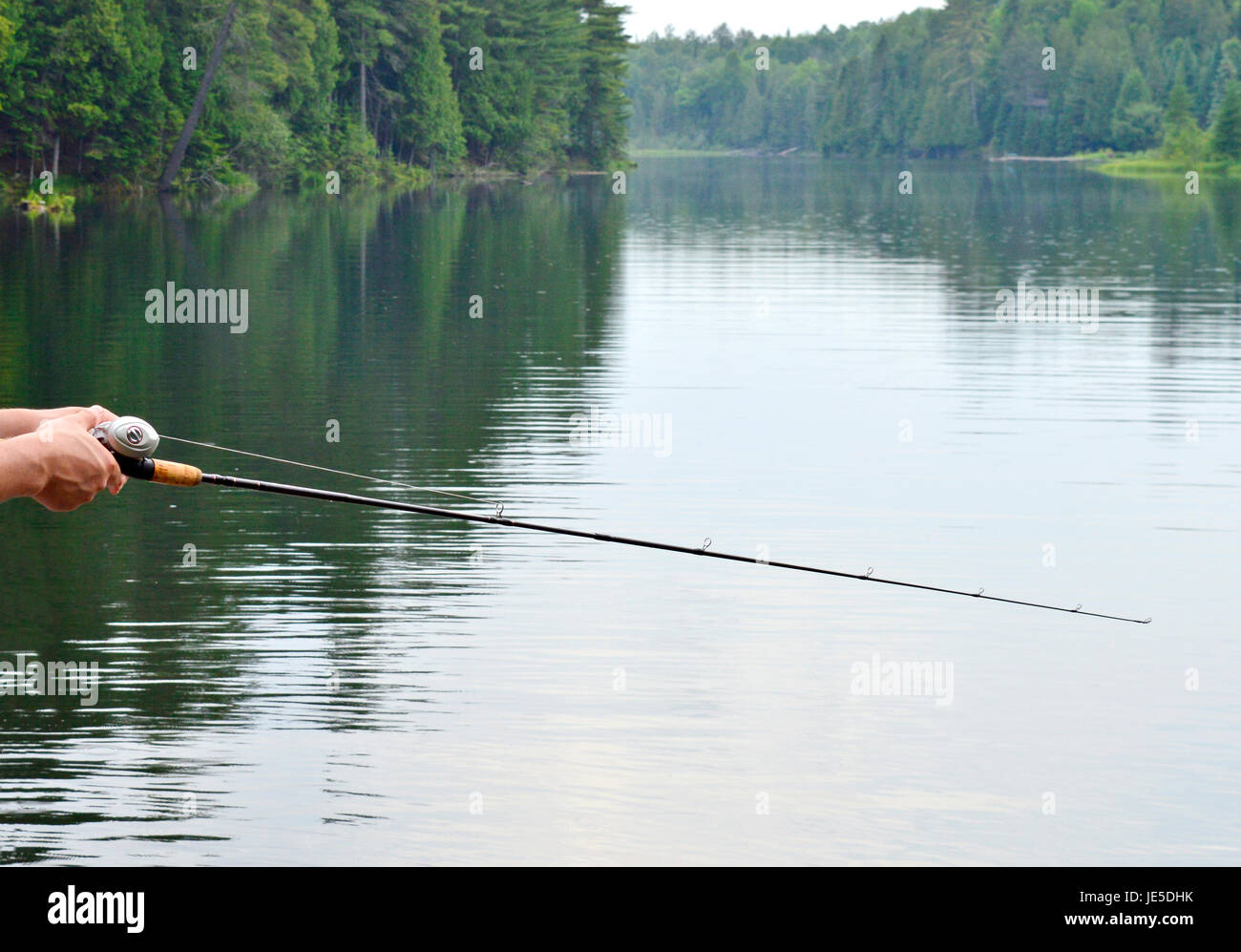 Un pescatore o donna getta in acqua di un calmo lago canadese Foto Stock