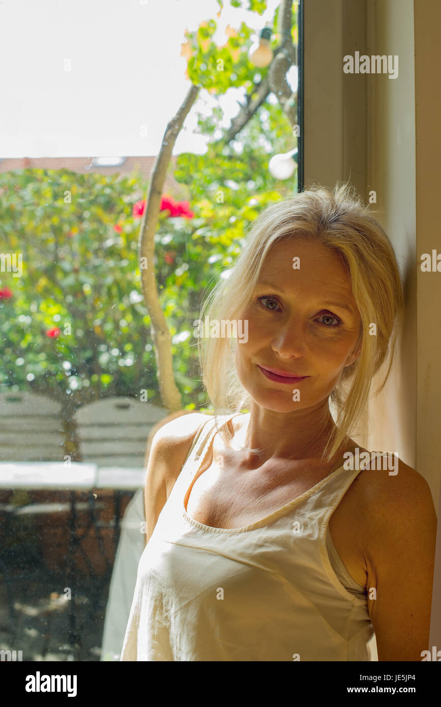 Donna matura appoggiata contro la finestra, ritratto Foto Stock