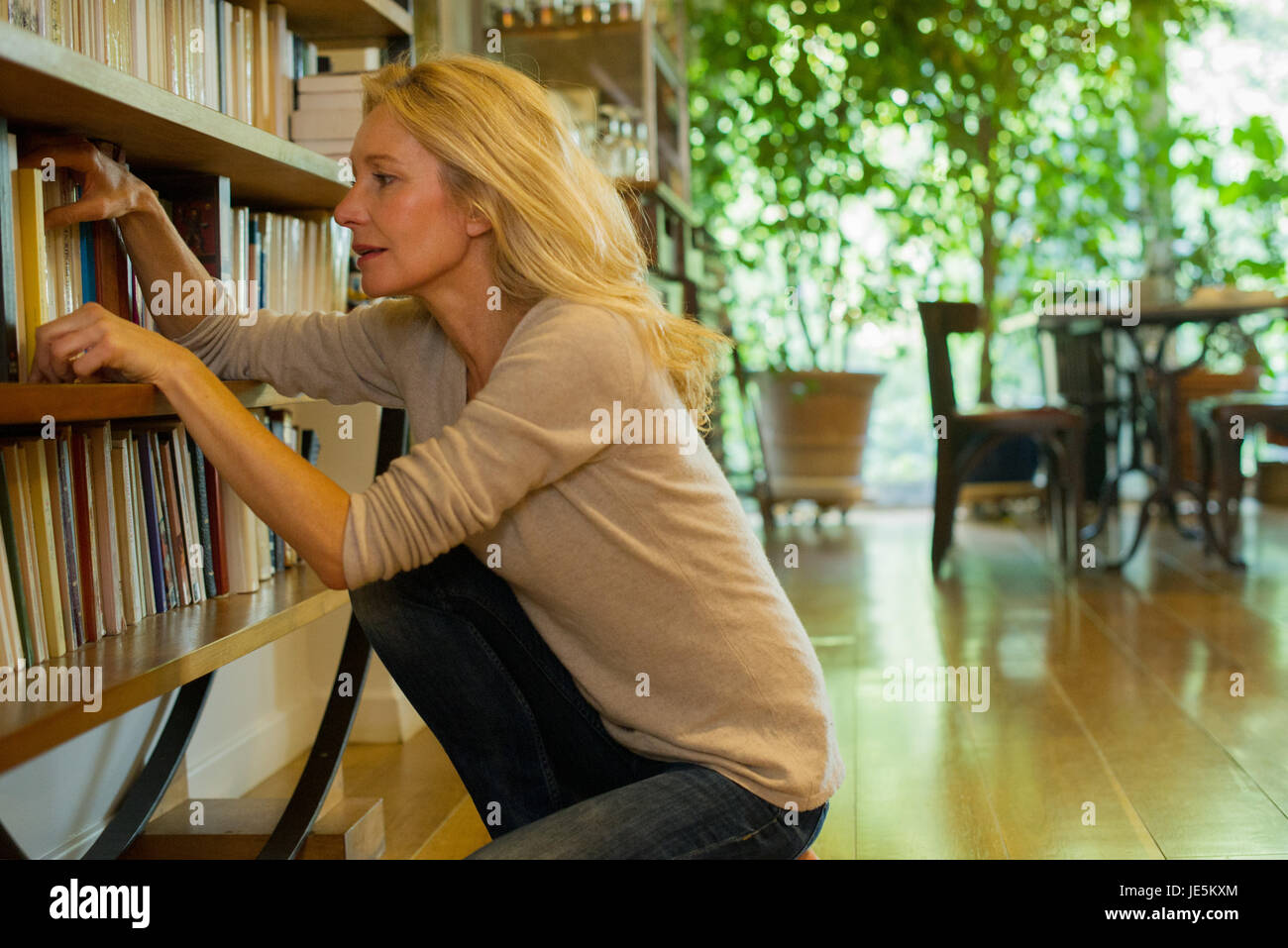 Donna matura guardando libri sullo scaffale a casa Foto Stock