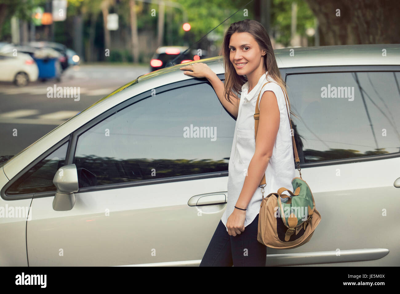 Giovane donna appoggiata contro auto, sorridente Foto Stock