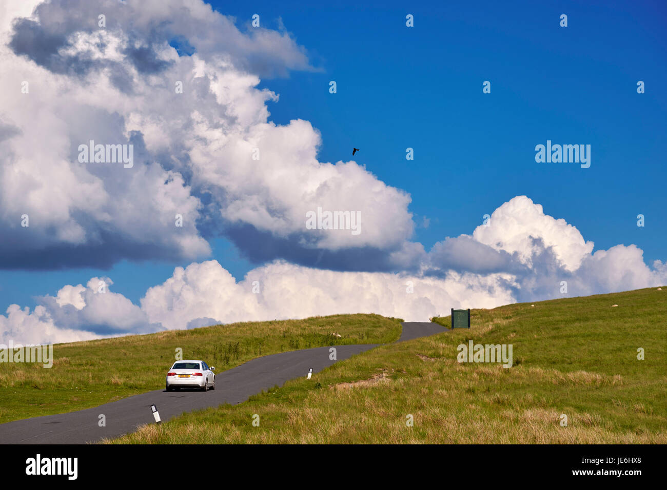 Auto sulla strada vicino alla valle di Elan serbatoi con un aquilone rosso volare al di sopra. Rhayader, POWYS, GALLES. Foto Stock