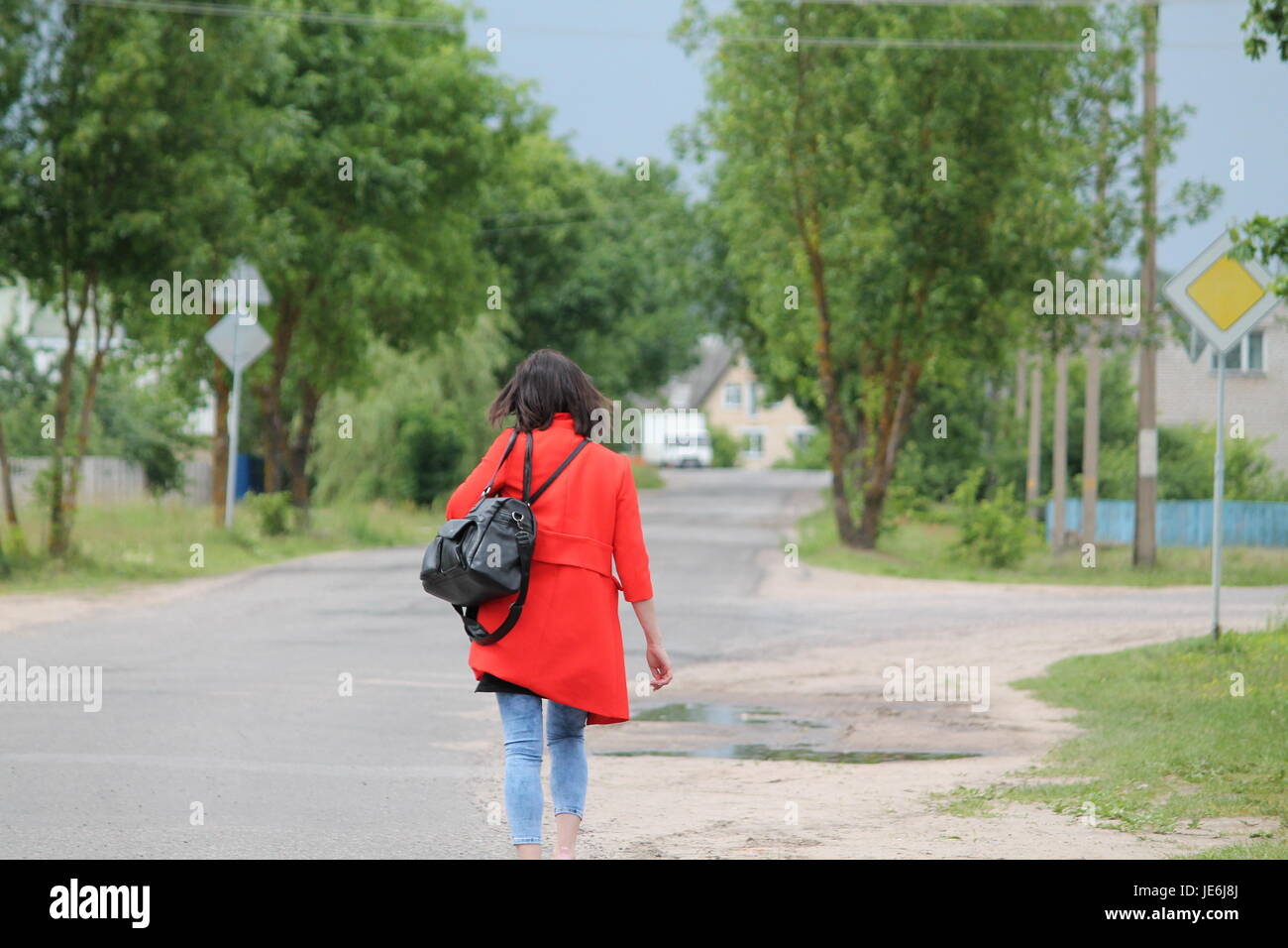 Giovani capelli scuri woman in red coat camminata veloce in estate verde vicolo Foto Stock
