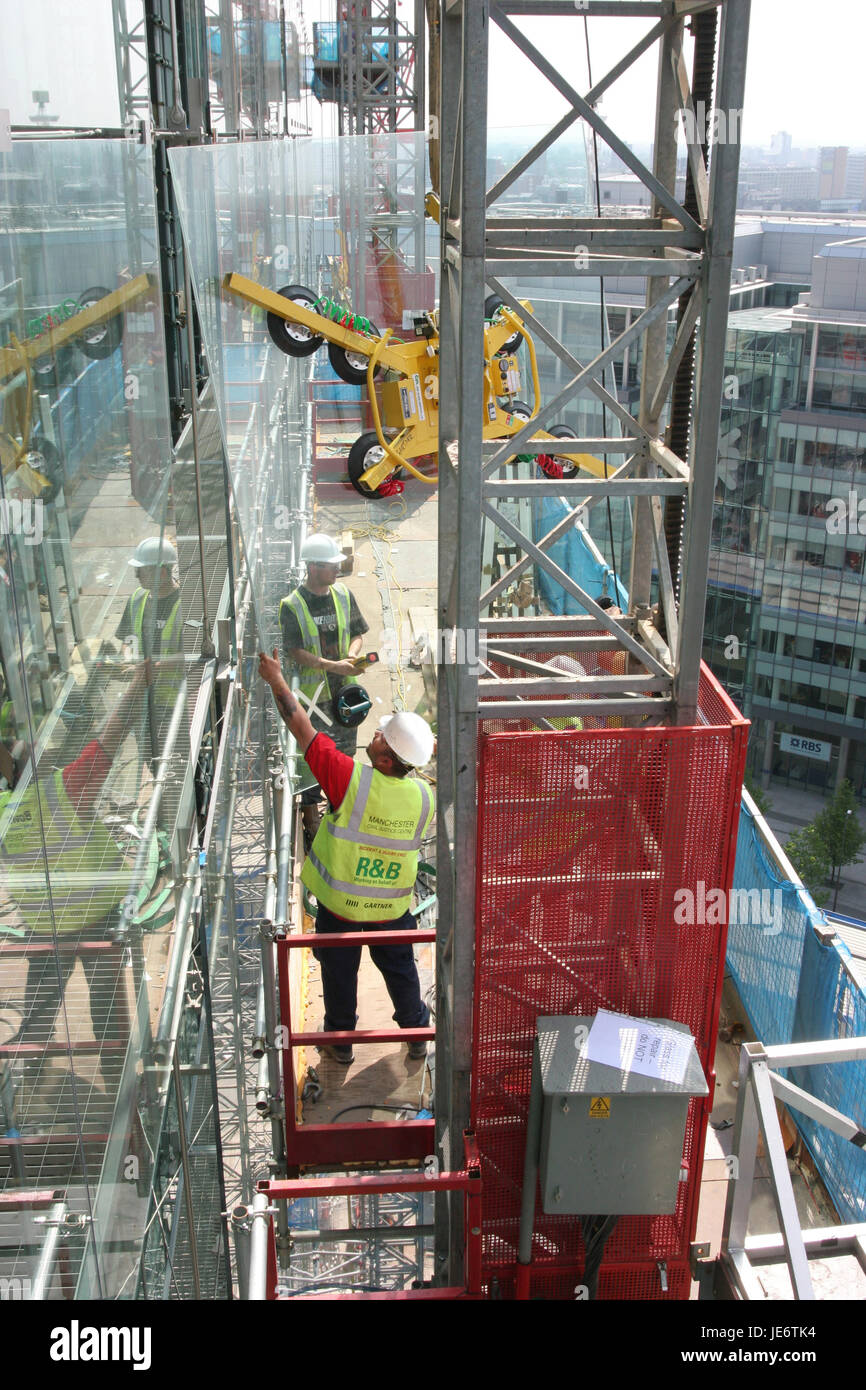 I contraenti montare i vetri esterni di un edificio alto con un albero elettrico di arrampicata su piattaforma di accesso e controllate a distanza supporto in vetro Foto Stock