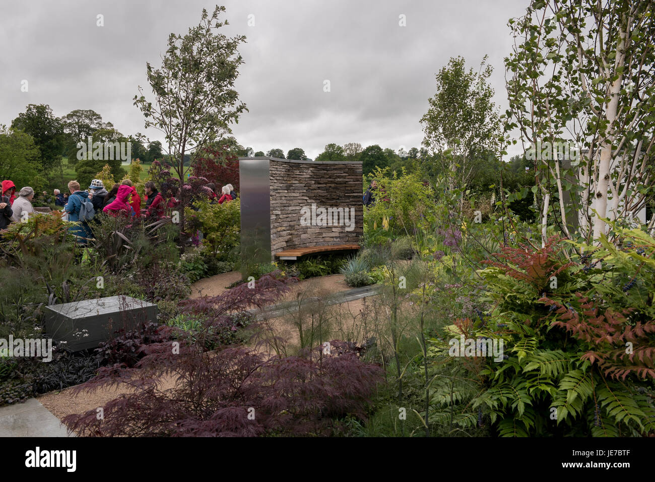 Gli ospiti passano tranquilla e appartata area con posti a sedere e piante in un giardino mostra in prima RHS Chatsworth Flower Show, la Chatsworth House, Derbyshire, Inghilterra, Regno Unito. Foto Stock
