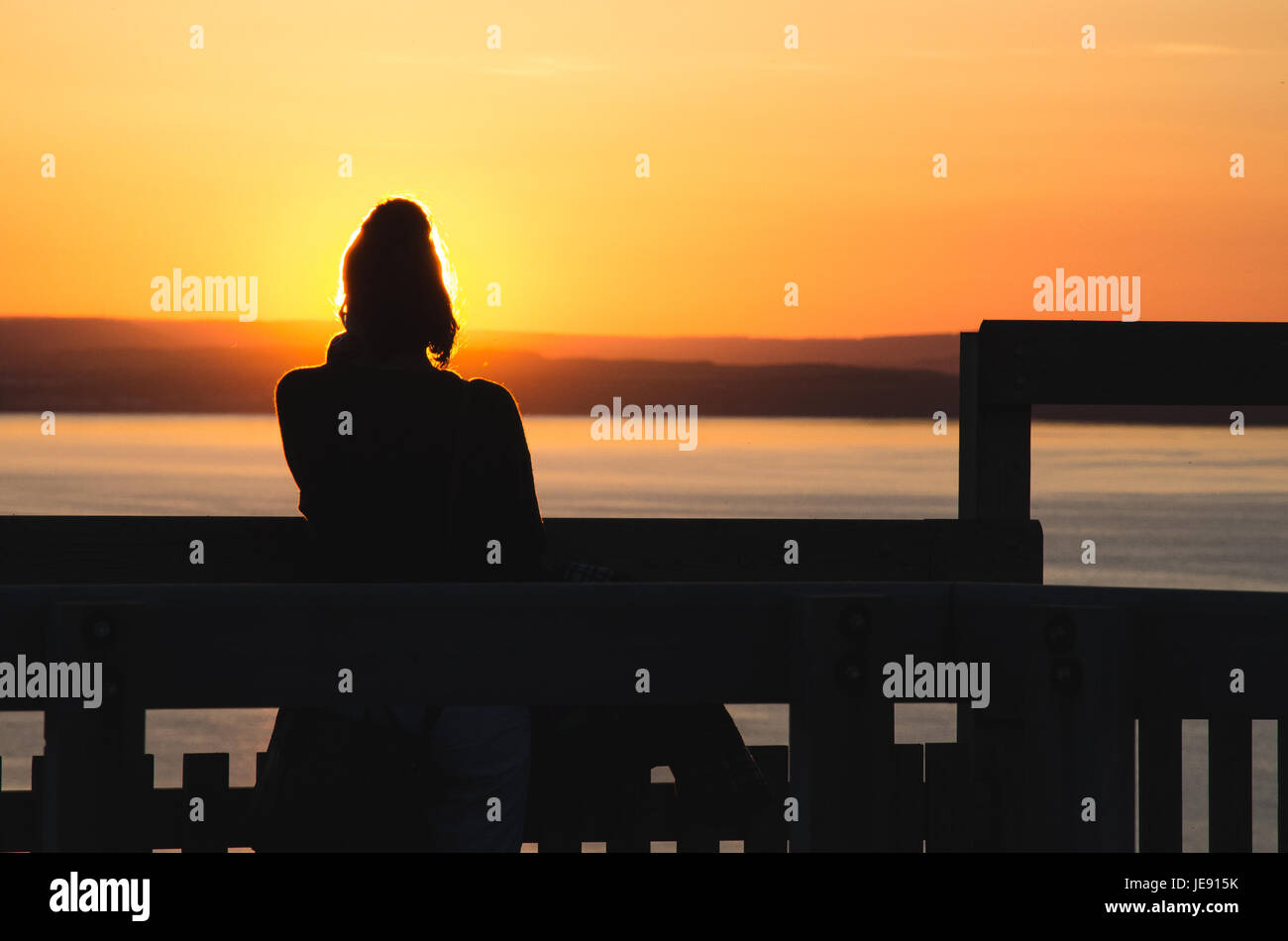 Silhouette di una donna che guarda al mare al tramonto. Foto Stock