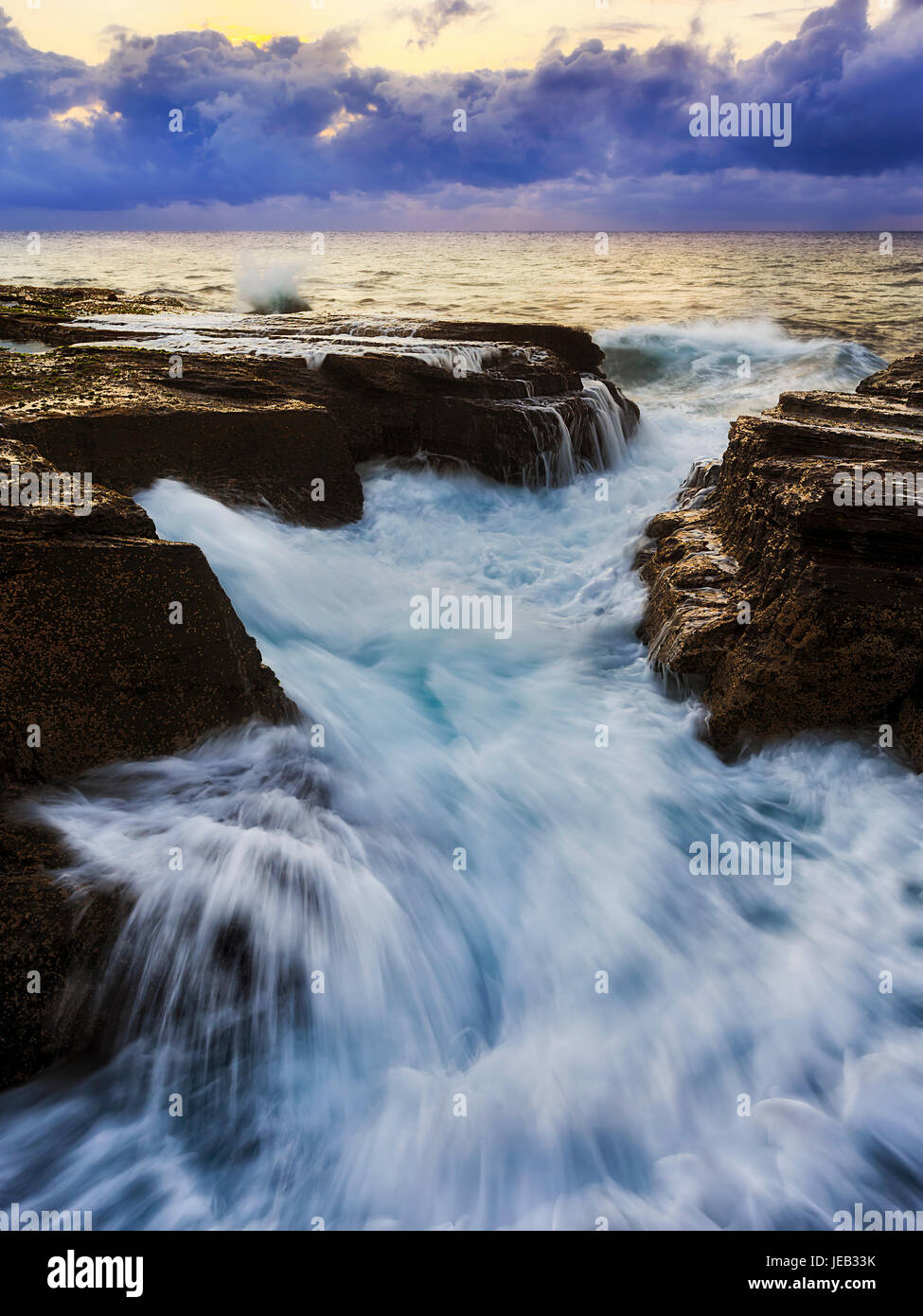 Fast forte ondata di acqua oceanica hits crack in costiera di rocce di arenaria a sunrise vicino Narrabeen spiaggia a nord di Sydney, Australia. Foto Stock